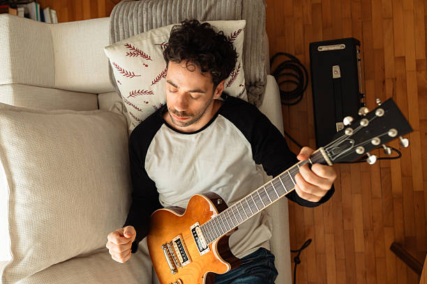 istock Young man lying on sofa and playing electric guitar at home 2233131062