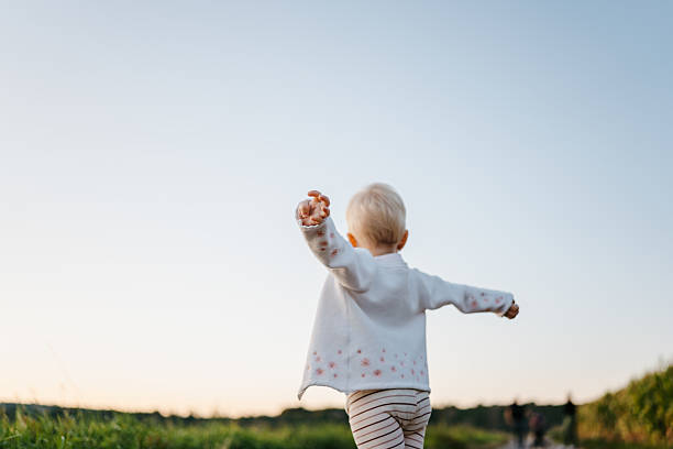 A 22-month-old girl raises her arms while walking freely along a countryside path. The playful movement captures joy, growth, and exploration.