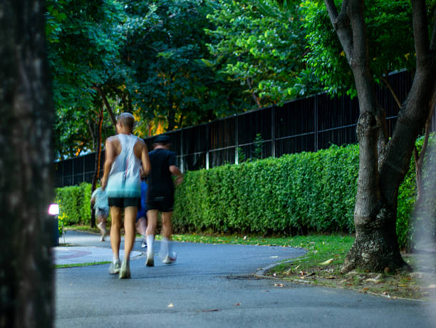 the legs of a runner in motion on a park path. The focus is on the lower half of the body, with athletic shoes and shorts visible as the person runs along a paved trail bordered by dirt and greenery.