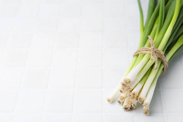 Bunch of fresh green onions on white tiled table. Space for text
