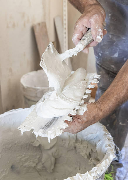 istock Craftsman spreads tile adhesive on notched trowel, dirty hands closeup. Construction process 2233134172