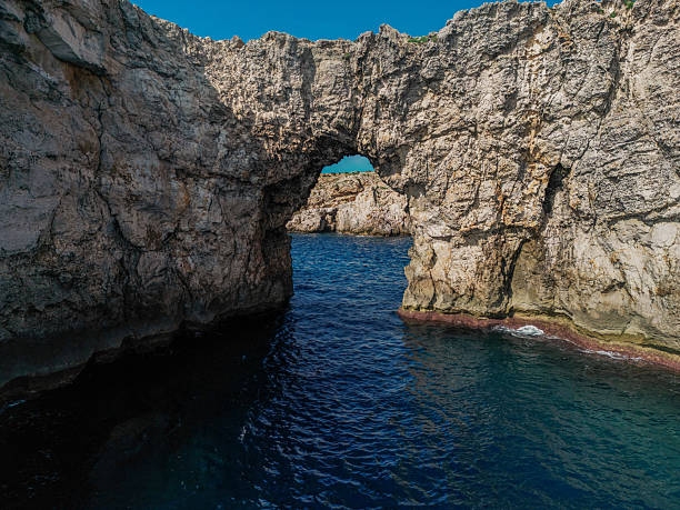 Massive stone arch rising above deep blue sea with rugged rocky cliffs
