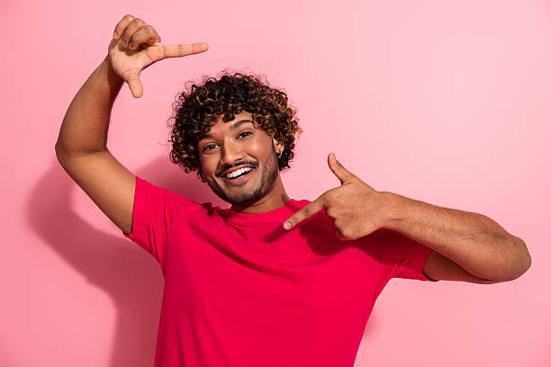 istock Cheerful young man posing with confident gestures on vibrant pink background showcasing stylish red t-shirt 2233136759