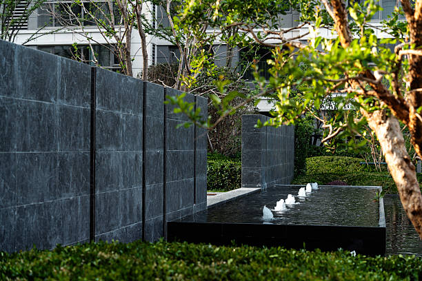 Elegant black granite water feature with multiple small fountains, surrounded by manicured green hedges in a modern residential landscape.