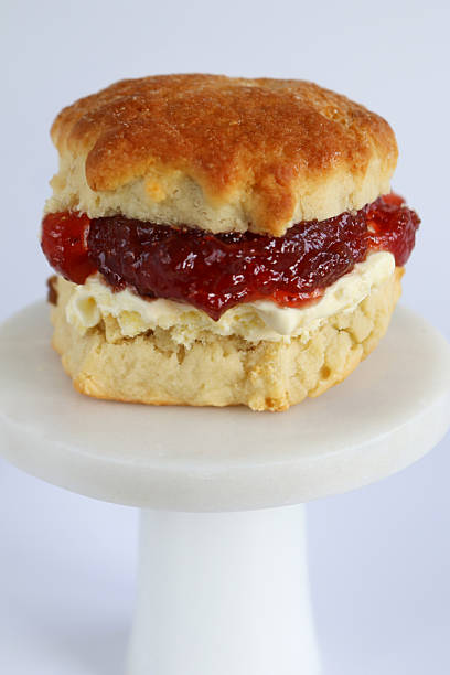 istock Image of classic white afternoon cream tea, fruit and plain scones with clotted cream, strawberry jam, served alongside cake, biscuit 2233138236