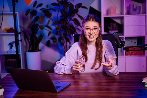 istock Young female podcaster sharing thoughts with microphone and laptop in a neon-lit studio, engaging evening atmosphere 2233143012