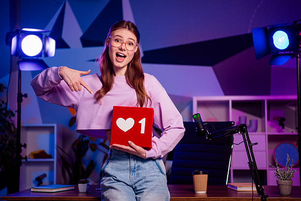 istock Young female vlogger holding a like icon and presenting content in a neon-lit studio with professional equipment 2233143270