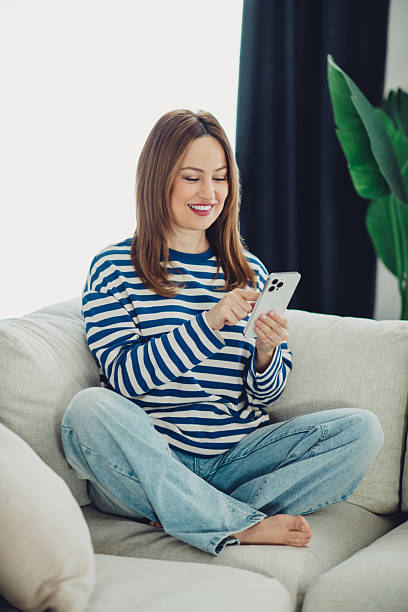 istock Young woman enjoying leisure time at home using her smartphone while sitting comfortably on a couch 2233145438