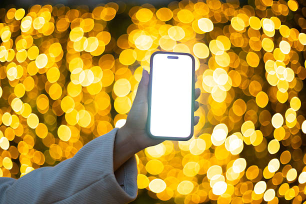 istock Hand holding smartphone against golden bokeh lights 2233148440