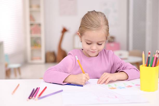 istock Cute girl drawing at white table in kindergarten 2233151178