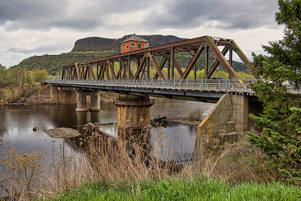 istock Historic iron bridge over a calm river with mountain backdrop. 2233151425