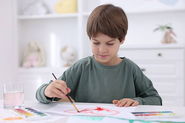 istock Cute boy drawing at white table in kindergarten 2233151471