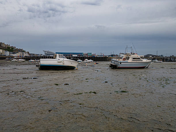 Scenic view of Granville port during low tide, with boats resting on sand and harbor walls exposed.