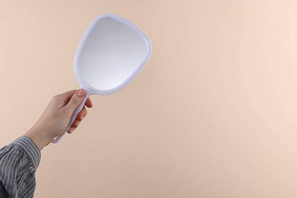 istock Woman holding handheld mirror on beige background, closeup. Space for text 2233153914
