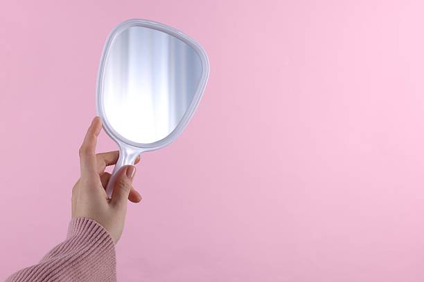istock Woman holding handheld mirror on pink background, closeup. Space for text 2233153925