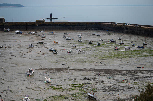 Granville, France - April 12, 2025: Scenic view of Granville port during low tide, with boats resting on sand and harbor walls exposed.