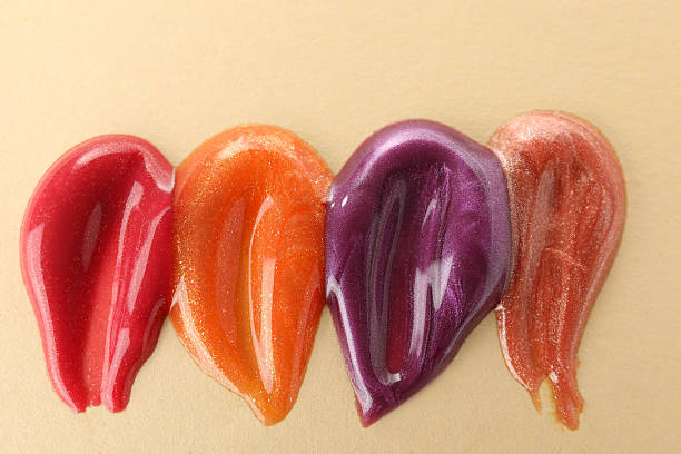 Samples of different lipglosses on beige background, top view