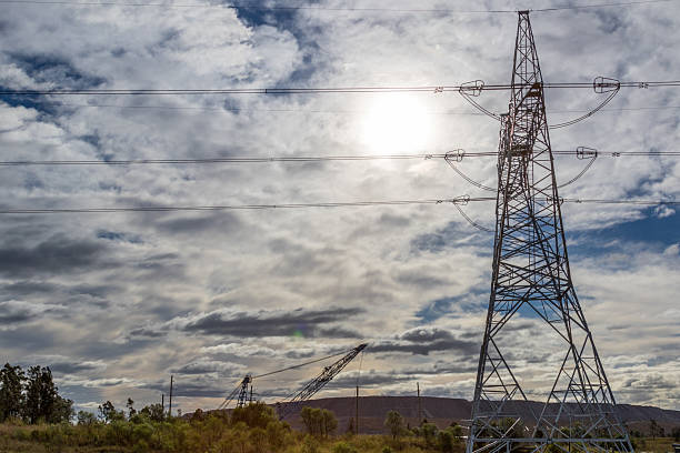 istock Lattice power transmission tower silhouetted against the sun breaking through a cloudy sky 2233159524