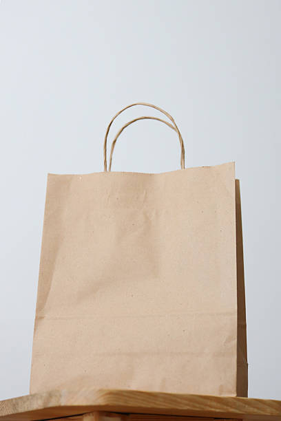 Plain brown paper bag on wooden surface with neutral background.