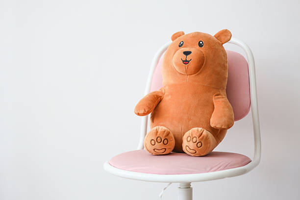 Cute brown teddy bear on pink chair in minimalist room setting