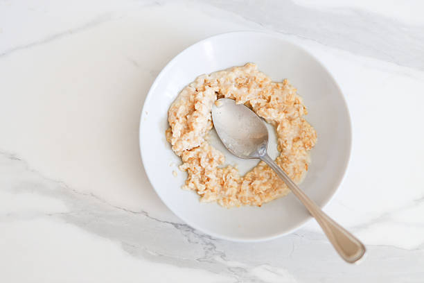 Creamy oatmeal breakfast in white bowl on marble surface with metal spoon.