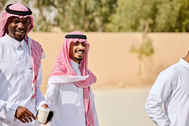 Cheerful Saudi businessmen walking at office courtyard during sunny day. Thoughtful male professionals are looking away outdoors. They are wearing kaffiyehs during break.
