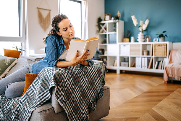 istock Young woman relaxing on sofa at home and reading book 2233166595