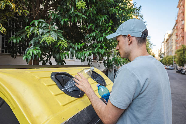 istock Young man in a cap recycling plastic bottles into a yellow container on a street in Rome, Italy, promoting sustainable living and environmental care. 2233170010