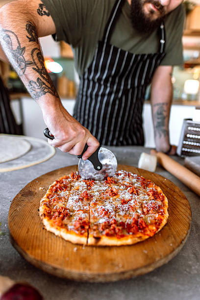 istock Chef cutting thin crust sausage pizza in kitchen with pizza cutter wheel. 2233176619