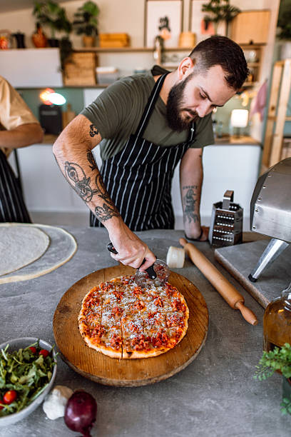istock Chef cutting thin crust sausage pizza in kitchen with pizza cutter wheel. 2233176628