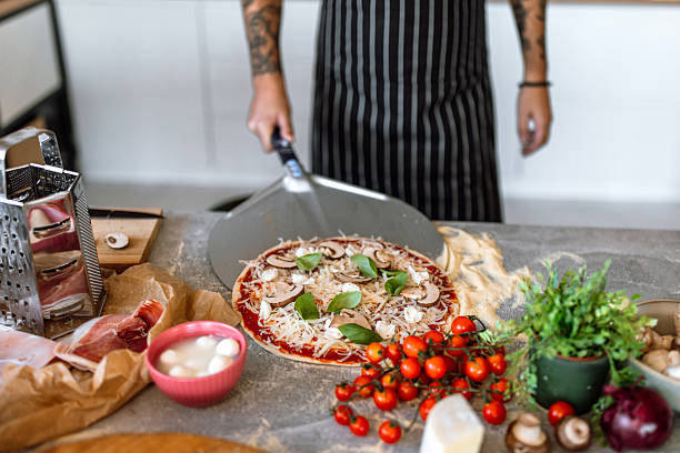 istock Young man in kitchen launching pizza in oven, using pizza shovel. 2233177041