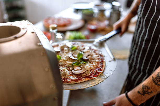 istock Young man in kitchen launching pizza in oven, using pizza shovel. 2233177082