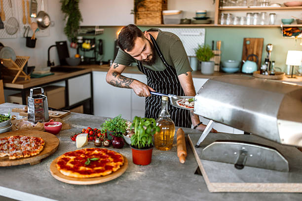 istock Young man in kitchen launching pizza in oven, using pizza shovel. 2233177095