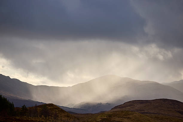 Sunlight peeking though the dark clouds on de trees an mountains, Glencoe, Scotland, UK