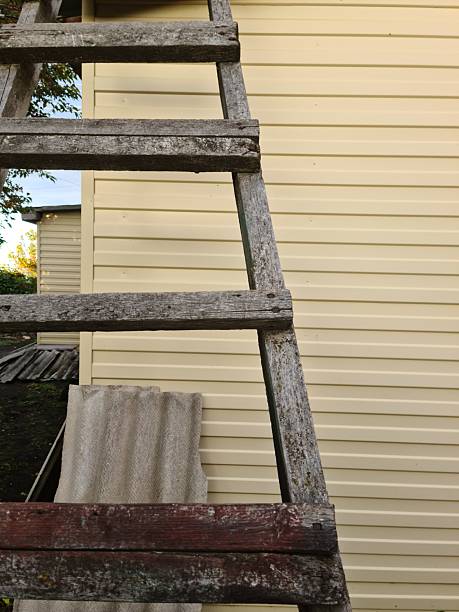 istock Weathered Wooden Ladder Leaning Against Light Siding Wall 2233178112