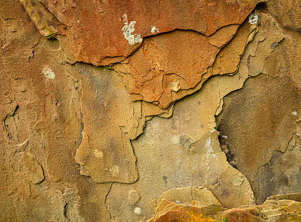 Part of an old gravestone seen in a churchyard in Suffolk, England. The stone is gradually crumbling away in layers of different colours.