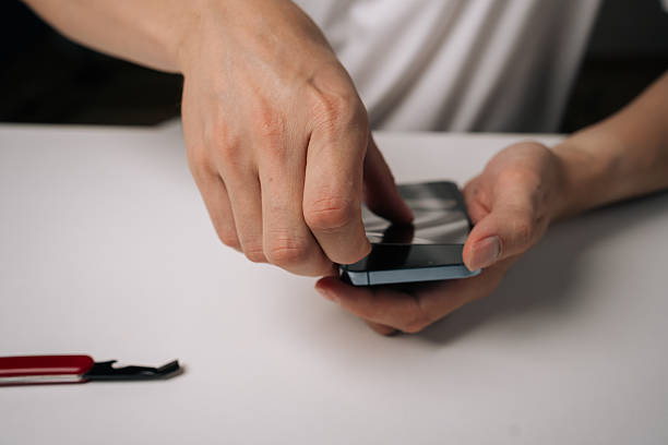 istock Skilled technician carefully removing damaged tempered glass screen protector from smartphone using precision repair tool, demonstrating professional device maintenance 2233185553