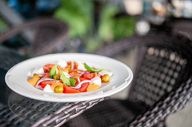 Fresh tomato, mozzarella, and basil salad served on a white plate outdoors. Vibrant ingredients, natural light, and relaxed dining atmosphere. Ideal for healthy food concepts