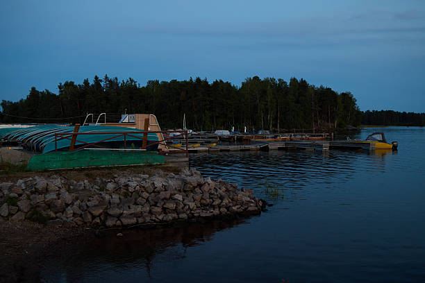 A picturesque lakeside view at dusk, featuring a charming dock, small boats, and lush trees as the sun sets