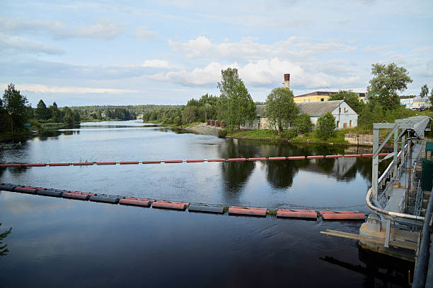 A serene view of a flowing river with floating barriers, surrounded by lush greenery and calm waters