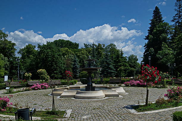 A beautiful relaxation area with a bench, a fountain and multi-colored bushes in bloom in the rose garden, Sofia, Bulgaria