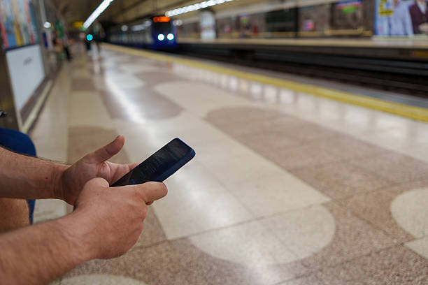 close up of hands holding smartphone while waiting for arriving subway train in madrid metro station, showcasing modern connectivity and urban lifestyle