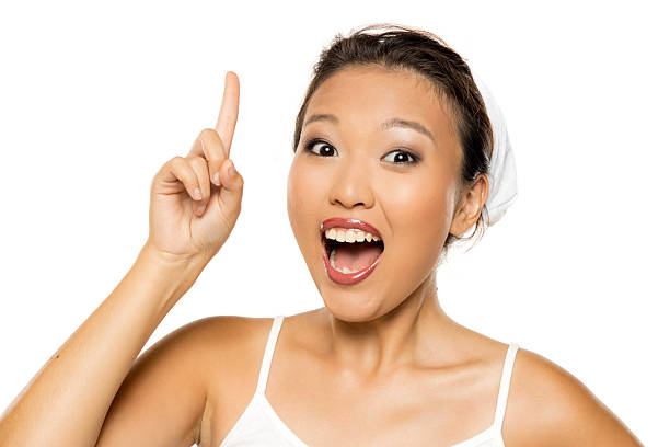 Smiling Asian woman with makeup pointing up with raised finger, studio shot on white background