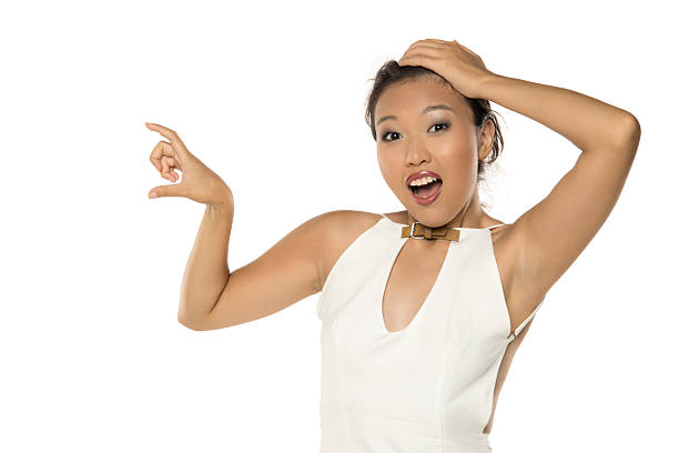 Surprised Asian woman holding tiny invisible product with fingers, studio shot on white background