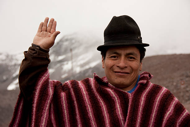Chimborazo, Ecuador - November 3, 2012: Portrait of a smiling indigenous Ecuadorian man wearing a poncho and hat, raising his hand in greeting with Chimborazo Volcano in the background