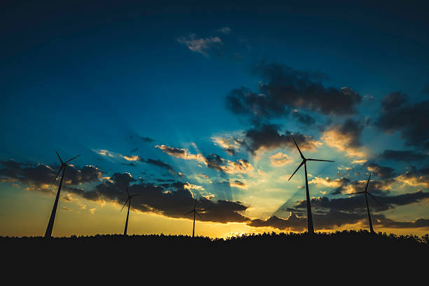 Silhouettes of wind turbines during a golden sunset with scattered clouds and colorful sky, symbolizing renewable energy sources and environmental harmony. The serene view portrays tranquility and sustainability.
