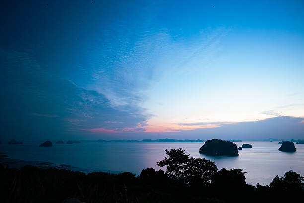 Peaceful early morning scene with soft blue and pink light illuminating tropical islands and calm sea before sunrise.