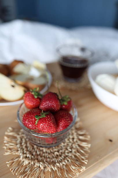 A warm breakfast-in-bed setup on a wooden tray featuring flaky croissants, sliced pear with creamy brie, fresh strawberries, a glass of coffee, and vanilla ice cream cones in soft natural window light, styled with a checkered linen for a minimalist Scandinavian home vibe and slow weekend lifestyle content