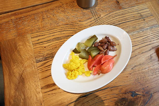 Rustic restaurant-style plate of colorful fermented vegetables including pink pickled radish, bright yellow cauliflower, crunchy dill cucumbers, and marinated onions on a wooden table, captured in warm natural light for healthy gut-friendly food and probiotic lifestyle themes.