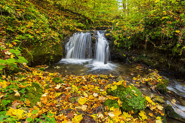 Beautiful waterfall cascading into a stream with autumn leaves covering the ground in Haj, Kosice Okolie District, Slovakia